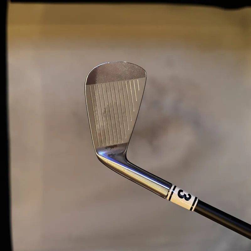 A seven-iron head with a numbered tag on the shaft, in front of an impact screen