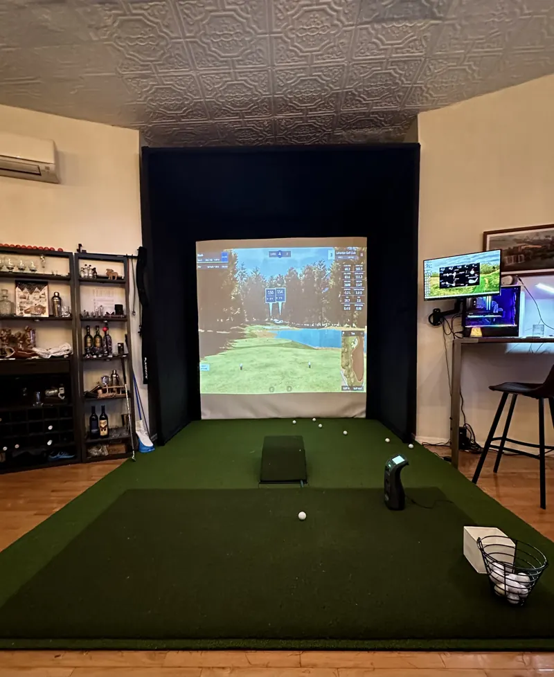 Indoor hitting bay with turf mat, launch monitor, and a projected golf course on the simulator screen